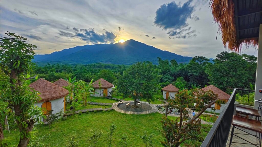 Vì Sao 90% Resort Chọn Rơm Nhân Tạo Làm Mái? Dự Án V Village Đà Nẵng Là Ví Dụ Điển Hình 1 Cảnh hoàng hôn buông xuống khu nhà mái rơm nhân tạo, với núi non phía xa.