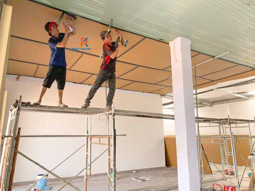 Hai thợ đang thi công trần bằng cót ép nhân tạo trong không gian nhà hàng lớn.