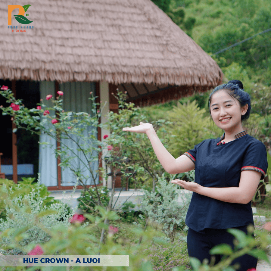 Rơm Nhân Tạo tại Hue Crown – A Lưới: Vẻ Đẹp Truyền Thống Trong Không Gian Nghỉ Dưỡng Xanh 2025 6 Du khách chụp ảnh bên khung nhà gỗ lợp rơm nhân tạo, nền trời chiều tạo hiệu ứng ánh vàng ấm áp – điểm nhấn du lịch sinh thái tại Huế.